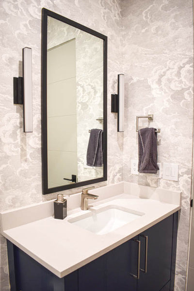 Interior design of bathroom with dark blue cabinets and light grey fun wallpaper. Designed by interior designer Erica LeMaster Sargent. 