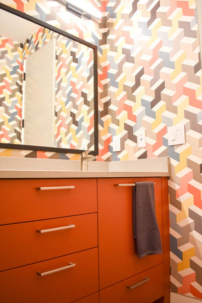 Interior design of bathroom with orange cabinet and colorful patterned wallpaper. Designed by interior designer Erica LeMaster Sargent. 