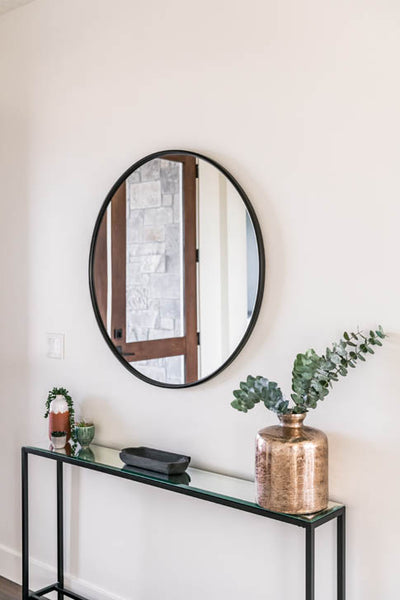 Interior design of main entryway with large circle mirror and black glass table. Designed by interior designer Erica LeMaster Sargent. 