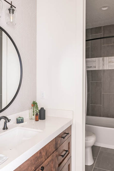 Interior design of bathroom with natural wood cabinets and large circle mirror. Designed by interior designer Erica LeMaster Sargent. 